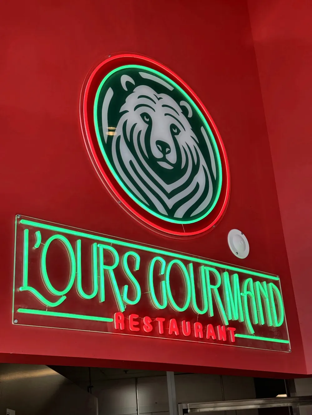 L'enseigne néon verte et rouge du restaurant, avec la tête d'ours et le lettrage L'Ours Gourmand.