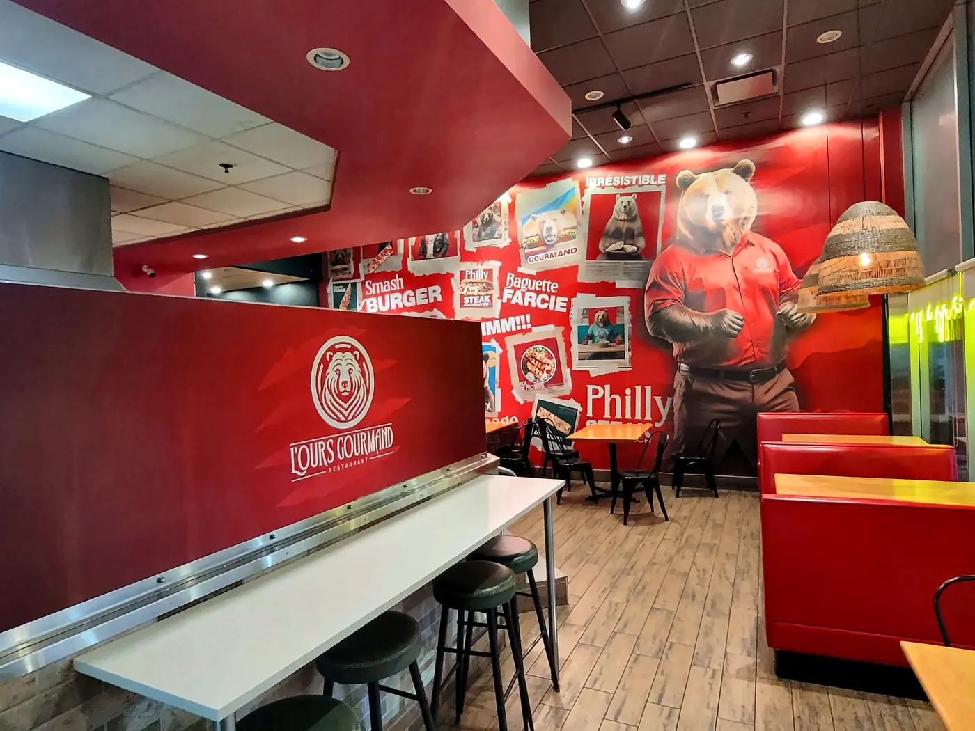 La salle à manger : comptoir rouge au logo de l'ours, tabourets, banquettes rouges et la grande murale avec l'ours en polo rouge.